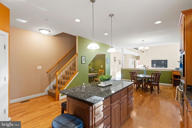 kitchen with light wood-type flooring, dark stone counters, hanging light fixtures, and a center island