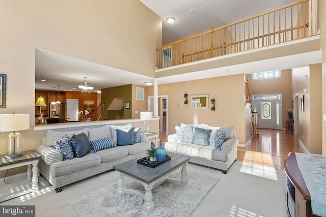 living room featuring a high ceiling, decorative columns, a notable chandelier, and light hardwood / wood-style floors