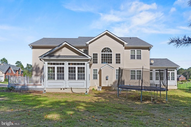 rear view of house featuring a sunroom, a deck, a trampoline, and a lawn