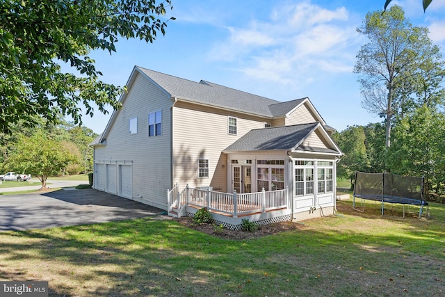 back of house with a yard, a wooden deck, a trampoline, and a garage