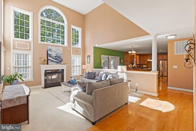 living room featuring a towering ceiling, decorative columns, and light hardwood / wood-style flooring