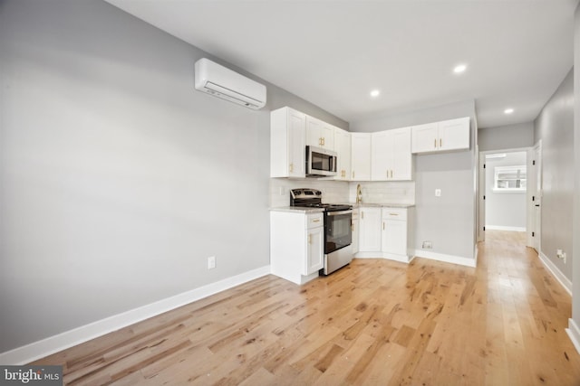 kitchen featuring tasteful backsplash, appliances with stainless steel finishes, white cabinetry, light hardwood / wood-style floors, and a wall unit AC