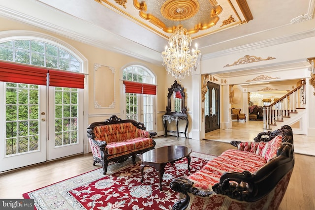 interior space with a raised ceiling, french doors, a notable chandelier, light wood-type flooring, and crown molding