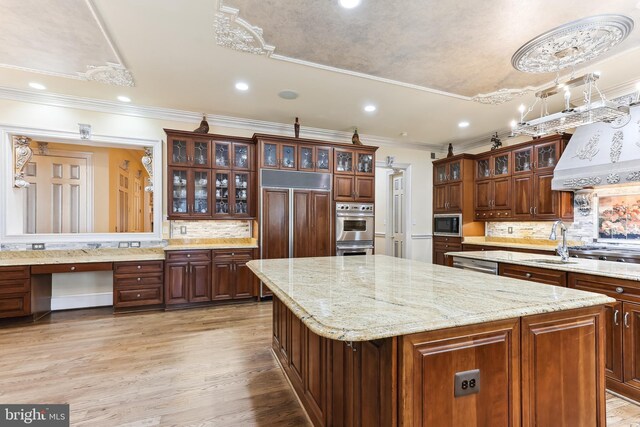 kitchen with tasteful backsplash, built in appliances, a center island, light hardwood / wood-style flooring, and sink