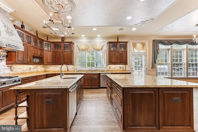 kitchen featuring ornamental molding, sink, a center island with sink, decorative light fixtures, and custom range hood