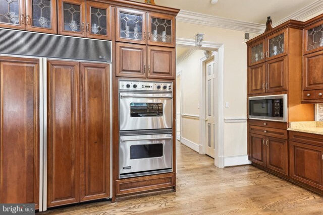 kitchen with light stone countertops, built in appliances, light wood-type flooring, and crown molding