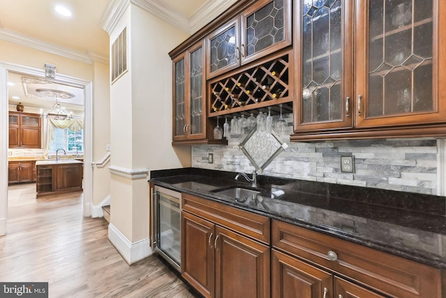 interior space featuring dark stone counters, light wood-type flooring, sink, beverage cooler, and ornamental molding