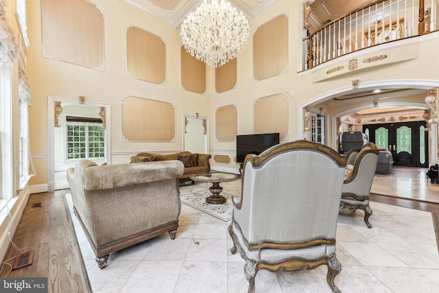 living room featuring light wood-type flooring, crown molding, a high ceiling, and a chandelier