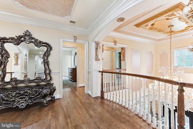 hallway with wood-type flooring, an inviting chandelier, a tray ceiling, and crown molding