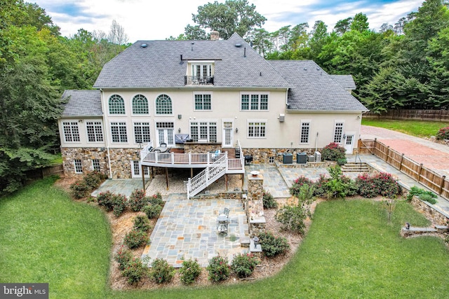 rear view of property with a deck, a lawn, and a patio