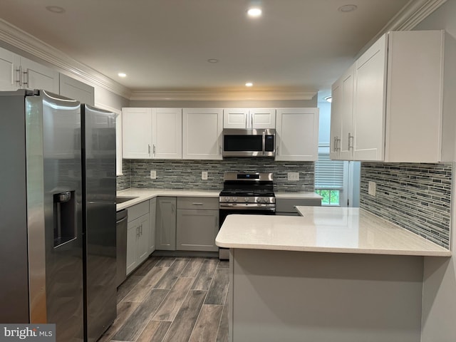 kitchen with kitchen peninsula, appliances with stainless steel finishes, dark wood-type flooring, and crown molding