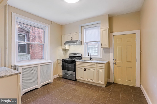 kitchen featuring dark tile patterned flooring, backsplash, stainless steel gas range, radiator, and sink