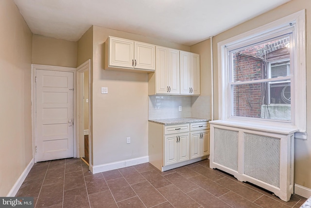 kitchen with dark tile patterned floors, radiator, light stone counters, and tasteful backsplash