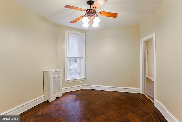 empty room featuring ceiling fan, dark parquet flooring, and radiator heating unit