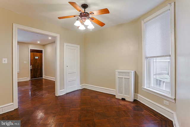 spare room featuring radiator heating unit, ceiling fan, and dark parquet flooring