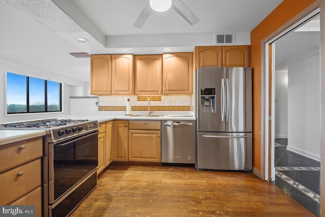 kitchen with appliances with stainless steel finishes, hardwood / wood-style floors, sink, backsplash, and ceiling fan