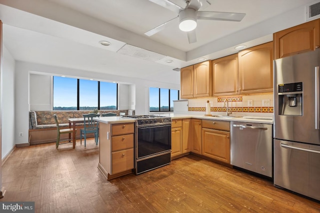 kitchen featuring appliances with stainless steel finishes, sink, decorative backsplash, kitchen peninsula, and light wood-type flooring