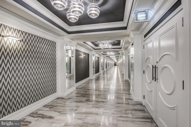 corridor with an inviting chandelier, a tray ceiling, and ornamental molding