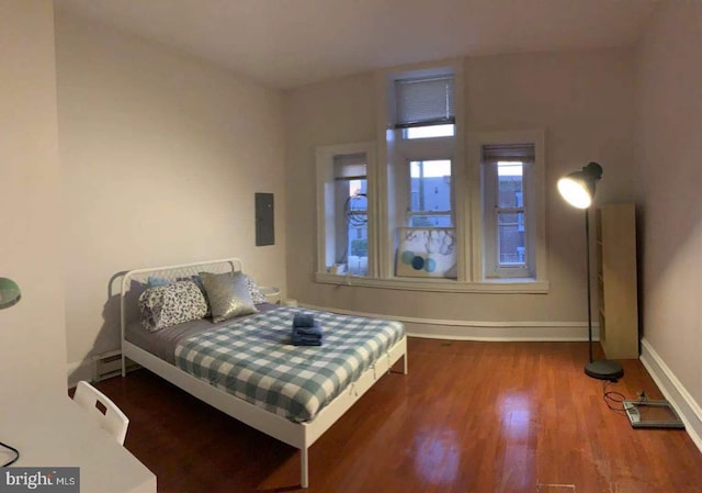 bedroom with electric panel, a baseboard heating unit, and hardwood / wood-style flooring