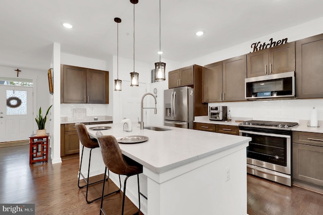 kitchen featuring a breakfast bar, an island with sink, hanging light fixtures, appliances with stainless steel finishes, and dark hardwood / wood-style flooring