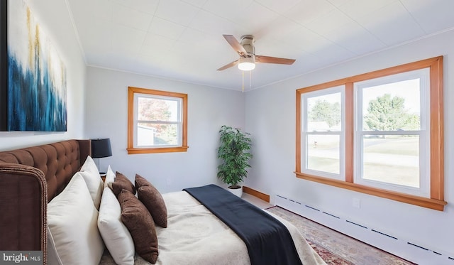 bedroom featuring a baseboard heating unit, multiple windows, ceiling fan, and crown molding