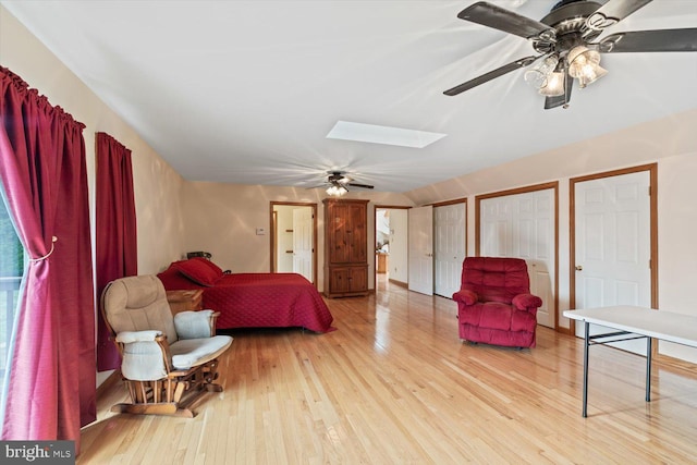 bedroom with vaulted ceiling with skylight, light hardwood / wood-style floors, ceiling fan, and multiple closets