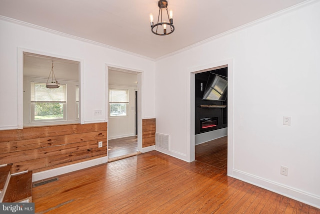 empty room featuring ornamental molding, a chandelier, and hardwood / wood-style flooring