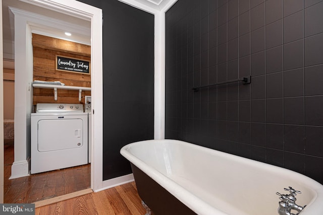 bathroom featuring a bathtub, washer / clothes dryer, wood walls, ornamental molding, and hardwood / wood-style floors