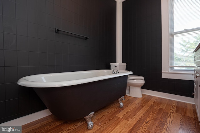 bathroom featuring a tub to relax in, hardwood / wood-style floors, tile walls, and toilet