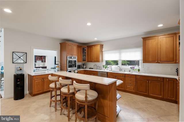 kitchen with sink, a kitchen island, a kitchen breakfast bar, appliances with stainless steel finishes, and light tile patterned floors