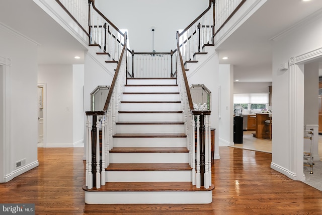 stairs featuring wood-type flooring, a high ceiling, and ornamental molding