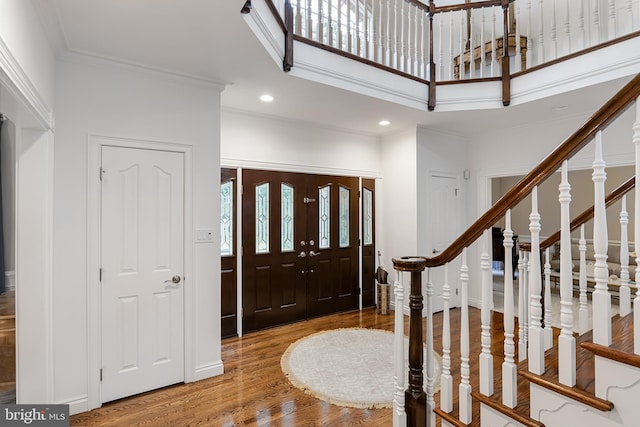 entryway featuring wood-type flooring, a towering ceiling, and crown molding