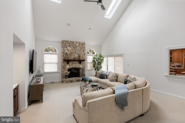 living room featuring high vaulted ceiling, a stone fireplace, ceiling fan, a skylight, and light colored carpet