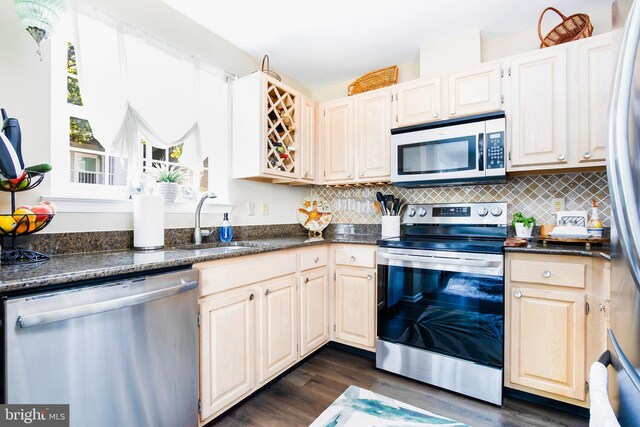 kitchen featuring dark stone counters, sink, backsplash, appliances with stainless steel finishes, and dark hardwood / wood-style flooring