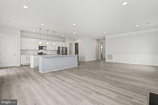 kitchen featuring appliances with stainless steel finishes, a center island with sink, light wood-type flooring, and white cabinets