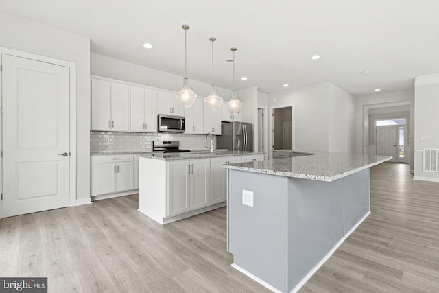 kitchen featuring an island with sink, stainless steel appliances, and white cabinetry