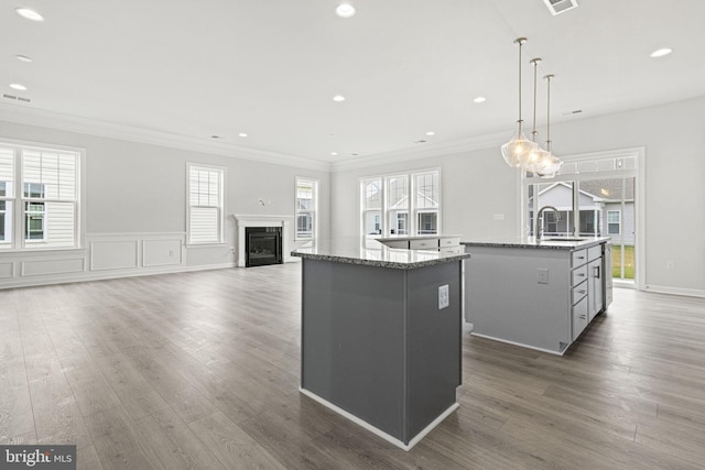 kitchen with hanging light fixtures, ornamental molding, sink, a center island with sink, and dark hardwood / wood-style floors