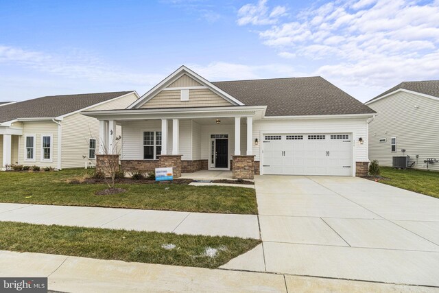 craftsman house featuring a porch, a garage, central air condition unit, and a front lawn