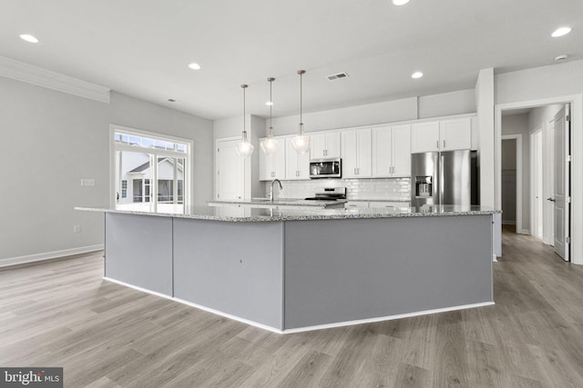 kitchen featuring white cabinets, appliances with stainless steel finishes, light wood-type flooring, and a large island with sink