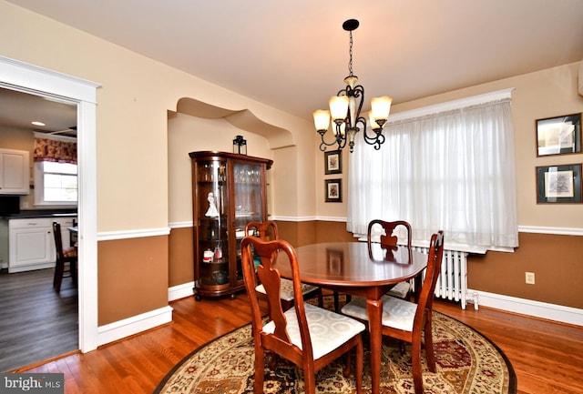 dining area with dark wood-type flooring, an inviting chandelier, and radiator heating unit