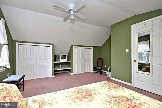 unfurnished bedroom with ceiling fan, multiple closets, carpet flooring, and vaulted ceiling