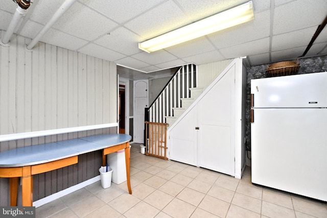 basement featuring a paneled ceiling and white refrigerator