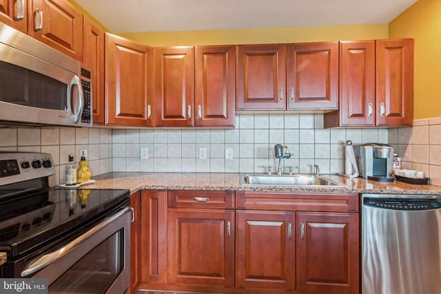 kitchen featuring light stone countertops, backsplash, appliances with stainless steel finishes, and sink