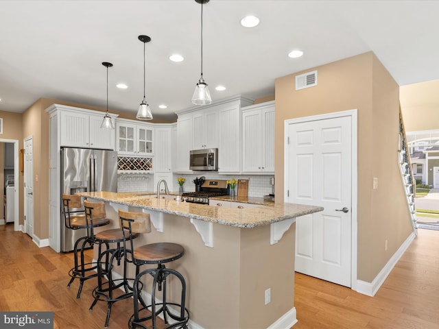 kitchen with pendant lighting, light hardwood / wood-style floors, white cabinets, a kitchen bar, and stainless steel appliances