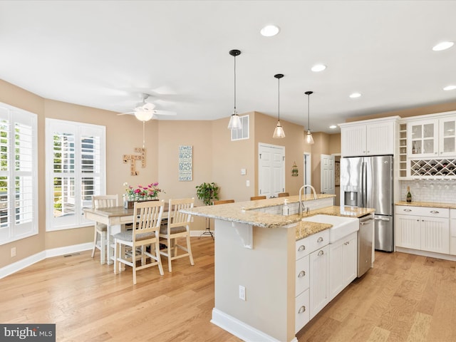 kitchen featuring an island with sink, white cabinets, stainless steel appliances, light hardwood / wood-style flooring, and sink