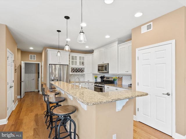 kitchen featuring light hardwood / wood-style flooring, stainless steel appliances, white cabinets, and a center island with sink