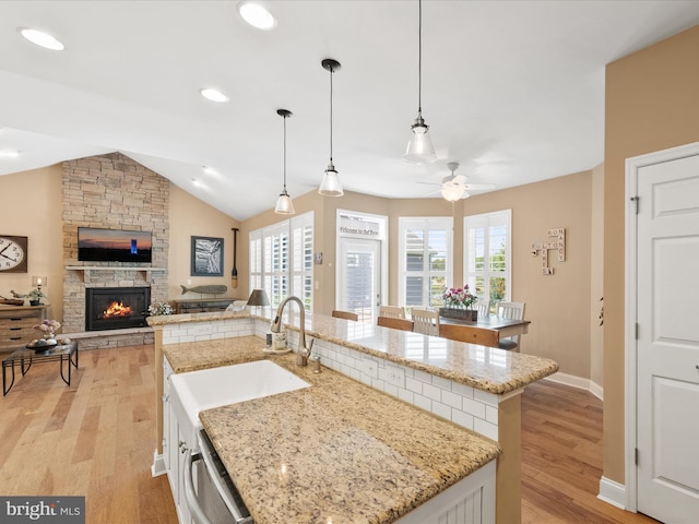 kitchen with a center island with sink, a stone fireplace, ceiling fan, and light hardwood / wood-style flooring