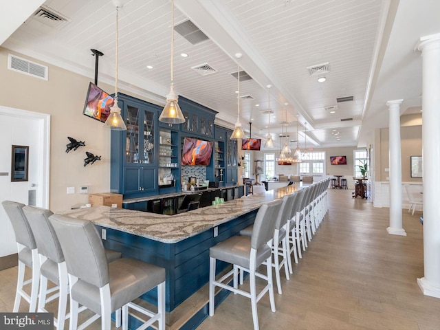 kitchen featuring blue cabinets, decorative light fixtures, decorative columns, light stone countertops, and a kitchen bar