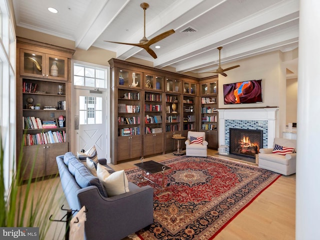 living room featuring a fireplace, ceiling fan, beamed ceiling, and light hardwood / wood-style flooring