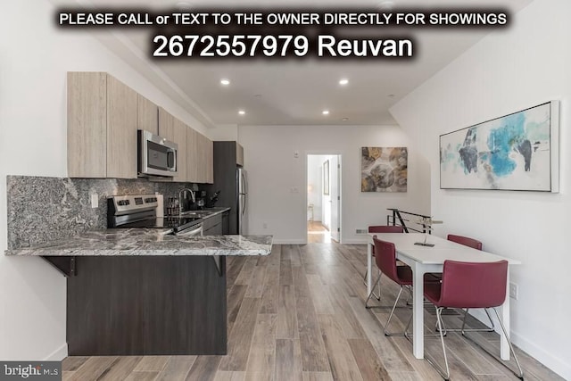 kitchen with light stone counters, kitchen peninsula, light hardwood / wood-style flooring, stainless steel appliances, and decorative backsplash